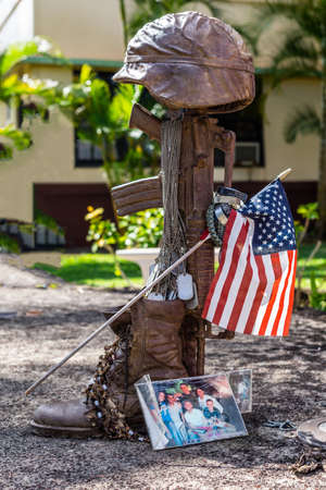 Oahu, Hawaii, USA. - January 10, 2012: Bronze helmet on rifle fallen soldier statue as part of United In Sacrifice group statue at Schofield Barracks of Army 25th Infantry Division. Flag, picture and green vegetation.のeditorial素材