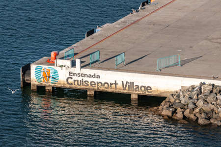 Ensenada, Mexico - January 17, 2012: Cruiseport Village sign on side of quay above blue bay water.