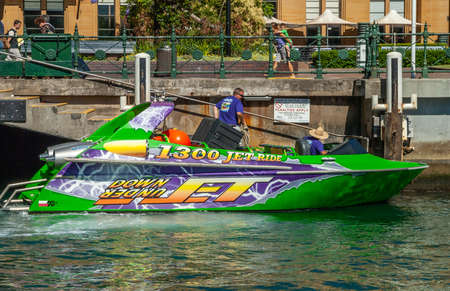 Sydney, Australia - December 11, 2009: Closeup of multi-color speed boat ready to leave pier with people, called 1300 Jet Ride. People on quay and green vegetation.のeditorial素材