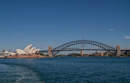 Sydney, Australia - December 11, 2009: Opera House with full black Harbour bridge and its anchor towers over deep blue bay water and under lighter blue sky.のeditorial素材