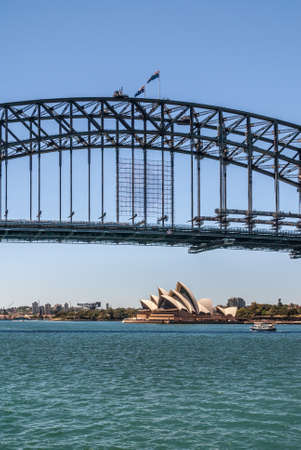 Sydney, Australia - December 11, 2009: Opera House seen under black Harbour bridge over azure bay water and under lighter blue sky.のeditorial素材