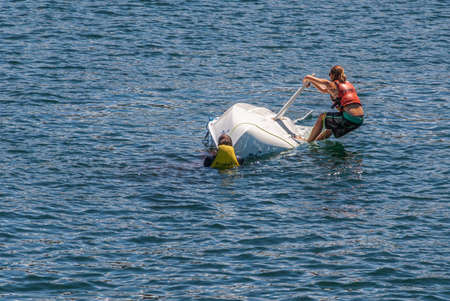 Sydney, Australia - December 11, 2009: Man and woman try manually to flip Capsized Magno Topaz small white sail boat back in dark blue bay water.のeditorial素材