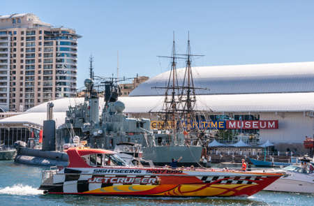 Sydney, Australia - December 11, 2009: Darling Harbour. High velocity Jet Cruiser passes ships on display in front of Maritime Museum building under light blue sky.のeditorial素材