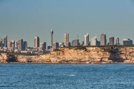 Sydney, Australia - December 11, 2009: City skyline with multiple skyscrapers seen from blue Tasman Sea with cliffs at gate into the bay under light blue sky and behind deep blue sea water.のeditorial素材