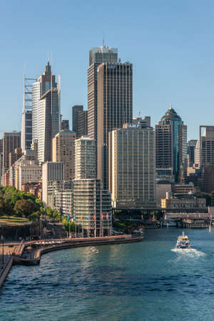 Sydney, Australia - December 11, 2009: Portrait Skyline AMP towers and others behind Circular Bay ferry terminal under light blue sky. Dark and azure water of bay with boats.のeditorial素材