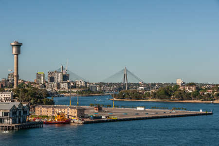 Sydney, Australia - December 11, 2009: Double suspension pylons of ANZAC Bridge with Millers Point in front set in dark blue bay water.  Green foliage in distance and blue sky.のeditorial素材