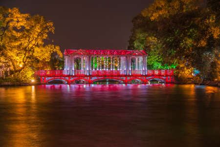 Guilin, China - May 9, 2010: Night photo. Glass or Crystal bridge under red light, and reflected in lake. Trees, some green and others orange in pitch dark night.の写真素材