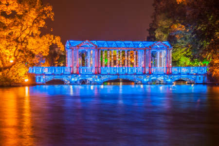 Guilin, China - May 9, 2010: Night photo. Closeup of Glass or Crystal bridge under blue light, and reflected in lake. Trees, some green and others orange in pitch dark night.の写真素材