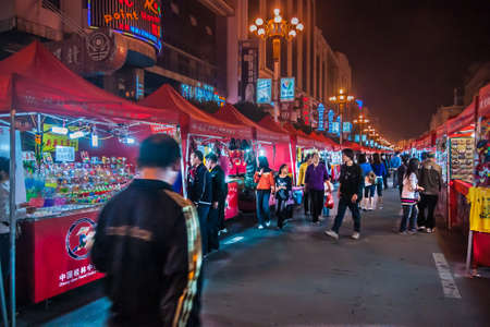 Guilin, China - May 9, 2010: Long shot through Zhong Shan Road evening market. Red booths strongly lighted inside under pitch black sky. Many shoppers wandering around.のeditorial素材