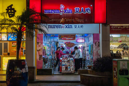 Guilin, China - May 9, 2010: Zhengyang pedestrian shopping street. Deep red light backdrop for blue-lighted Nuren Xin name of lingerie boutique. People making their choices in store.のeditorial素材