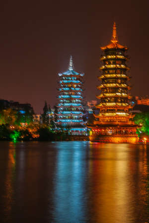 Guilin, China - May 9, 2010: Riyue Shuangta Cultural Park. The  Twin Pagodas in Shanhu Lake, the silver and the gold, under pitch black night. Their lights reflected in water. Other lights on shore.の写真素材