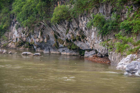 Guilin, China - May 10, 2010: Along Li River. Green foliage covers partly opening to cave in...