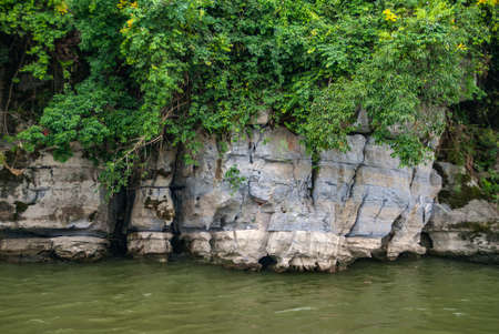 Guilin, China - May 10, 2010: Along Li River. Closeup of cracked feed of forested gray-blue-black...