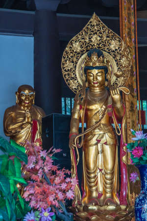 Guilin, China - May 11, 2010: Qixia Buddhist Temple in Seven Star Park. Closeup of golden statue of Guan Yin goddess. Flowers around and golden saint statue in back.のeditorial素材