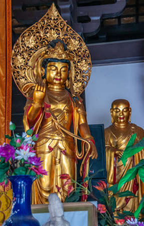Guilin, China - May 11, 2010: Qixia Buddhist Temple in Seven Star Park. Closeup of golden statue of Guan Yin goddess. Flowers around and golden saint statue in back.のeditorial素材