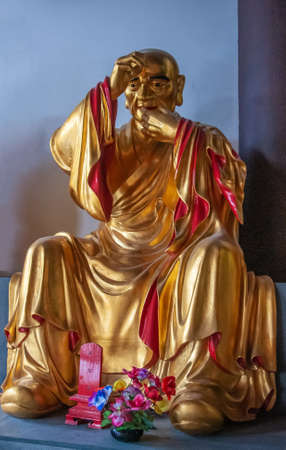 Guilin, China - May 11, 2010: Qixia Buddhist Temple in Seven Star Park. Golden statue of Joyous Arhat, Chinese Buddhist saint against blue blackdrop.のeditorial素材