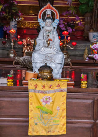 Guilin, China - May 11, 2010: Qixia Buddhist Temple in Seven Star Park. White statue of Guan Yin goddess with candles around her and yellow banner under her.のeditorial素材