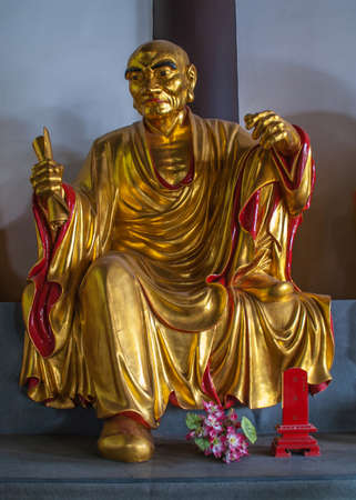 Guilin, China - May 11, 2010: Qixia Buddhist Temple in Seven Star Park. Golden statue of Arhat who holds roll of paper, JÃ¬nshÅ« LuÃ³hÃ n, Chinese Buddhist saint against blue blackdrop.のeditorial素材
