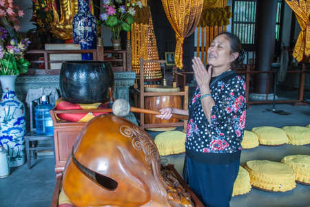 Guilin, China - May 11, 2010: Qixia Buddhist Temple in Seven Star Park. Woman announces her arrival by drumming on wooden statue in colorful and chaotic temple interieur.のeditorial素材