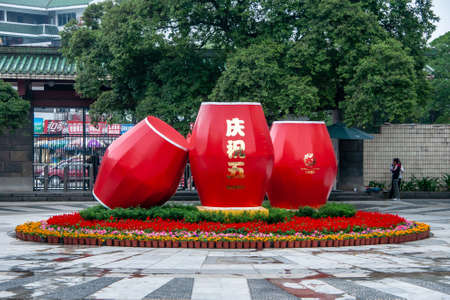 Guilin, China - May 11, 2010: Seven Star Park. Giant red drums statue set in red and orange flowers at entrance. Stret view behind through gate. Green foliage above.のeditorial素材