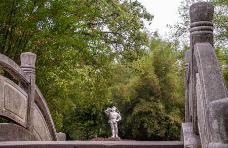 Guilin, China - May 11, 2010: Seven Star Park. White statue of boy in military uniform blowing the bugle in front of wall of green foliage as seen from over gray stone bow bridge.のeditorial素材