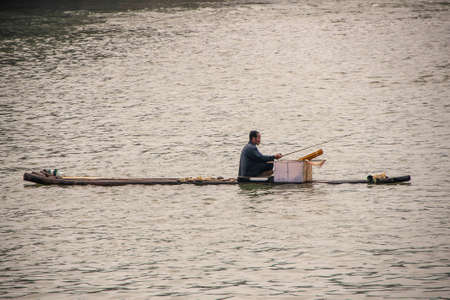 Guilin, China - May 11, 2010: Closeup of lone fisherman sitting on flimsy bamboo raft on silver Li river downtown.のeditorial素材