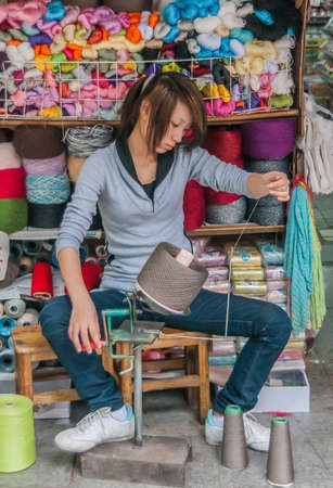 Guilin, China - May 11, 2010: Downtown. Young woman winds manually thread on spindle. Colorful...