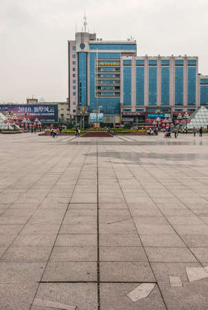 Guilin, China - May 10, 2010: Downtown Central Square. Portrait of Modern gray office building with blue glass walls under silver sky. Pyramids in glass, people and park square.のeditorial素材
