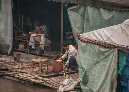 Guilin, China - May 11, 2010: Downtown. Migrant workers eating in their shack and tent like housing, built on rafts on Li River near shore.のeditorial素材