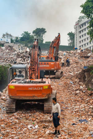 Chongqing, China - May 9, 2010: Downtown, off Peoples Square. Red Daewoo and Hitachi demolition craned on top of pile of stone rubble. Workers present.のeditorial素材