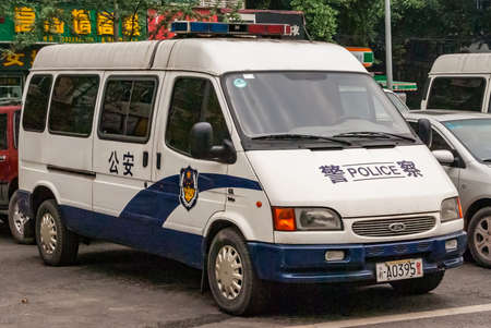 Chongqing, China - May 9, 2010: Downtown. Closeup of white parket Police van with green foliage in back. parts of other cars and yellow mandarin symbols on green.のeditorial素材