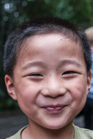 Chongqing, China - May 9, 2010: Inside zoo or animal park. Closeup of face of smiling pre-teen boy against dark green foliage backdrop.のeditorial素材