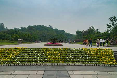Chongqing, China - May 9, 2010: Inside zoo or animal park. Large yellow, white and red flower beds in center of broad walkway just inside the zoo. Backdrop of green foliage under light blue sky.のeditorial素材