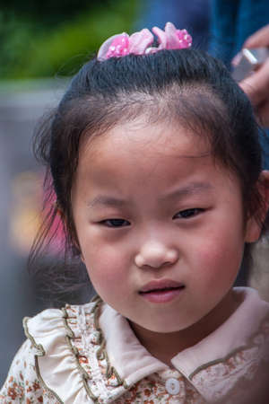 Shanghai, China - May 4, 2010: Closeup of face oif young girl with pink decoration in black hair and wearing fancy dress, holding a wondering and studying expression.のeditorial素材