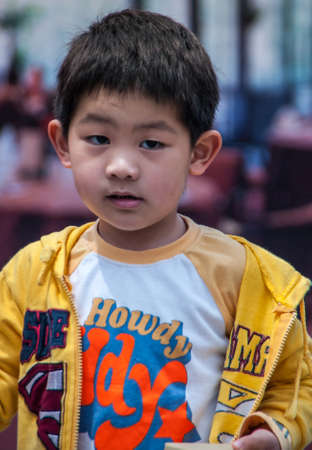 Shanghai, China - May 4, 2010: Closeup of boy wearing yellow vest and Howdy shirt looks puzzling into camera.のeditorial素材