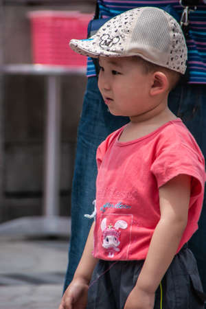 Shanghai, China - May 4, 2010: Closeup of boy wearing rose shirt and beige baseball cap, looking relaxed and observing.のeditorial素材