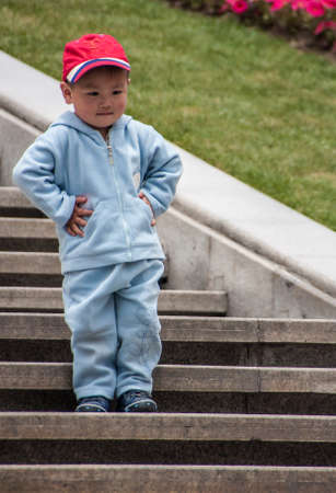 Shanghai, China - May 4, 2010: Closeup of young boy with red cap and light blue pants and vest, has...