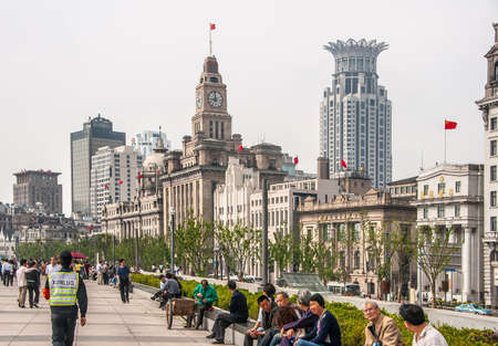 Shanghai, China - May 4, 2010: Huangpu river boardwalk with lots of people and row of historic financial buildings. Crowned one is Bund Financial Center Tower. Clock tower of Custom House.のeditorial素材