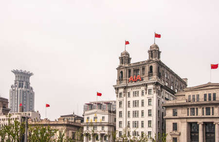 Shanghai, China - May 4, 2010: Historic building facades with red Chinese flags on top along Bund under silver sky. Far left with crown is Bund Financial Center Tower.のeditorial素材