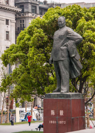 Shanghai, China - May 4, 2010: Massive gray statue on red pedestal of Chen Yi, first mayor, a man, with green foliage at his back. Parts of building facades and people around.のeditorial素材