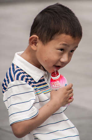 Shanghai, China - May 4, 2010: Closeup of boy child in white shirt sipping yoghurt out of red plastic bottle.のeditorial素材