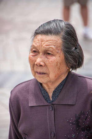 Shanghai, China - May 4, 2010: Closeup of face of older graying senior woman dressed in purple garb.のeditorial素材