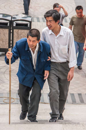 Shanghai, China - May 4, 2010: Young man in white shirt helps old man with bamboo cane and blue vest up the stairs.のeditorial素材