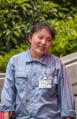 Shanghai, China - May 4, 2010: Closeup of young woman in blue shirt and with name and function badge. Green foliage in back.のeditorial素材