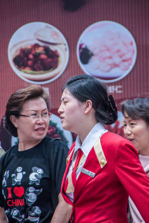 Shanghai, China - May 4, 2010: Three women engage and talk with each other while walking in front of restaurant while on which images of food dishes are advertised.のeditorial素材