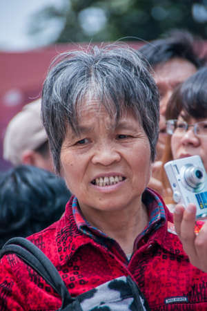 Shanghai, China - May 4, 2010: Portrait of woman with short graying hair and red vest holds silver camera, showing her teeth and in a struggling mood.のeditorial素材