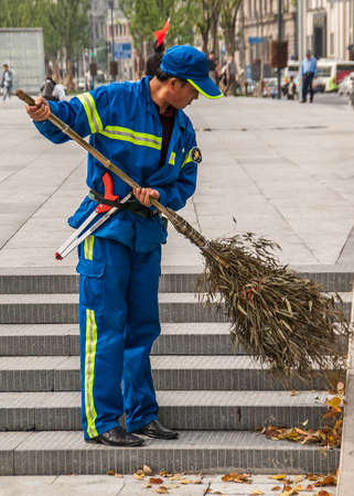 Shanghai, China - May 4, 2010: Worker street sweeper in blue uniform with yellow security ribbons...