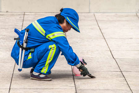 Shanghai, China - May 4, 2010: Worker street cleanier in blue with yellow security lines removes gum...