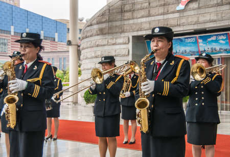 Shanghai, China - May 4, 2010: All female music band plays in front of gray stone wall on red carpet, blowing their brass instruments and dressed in black and gold.のeditorial素材