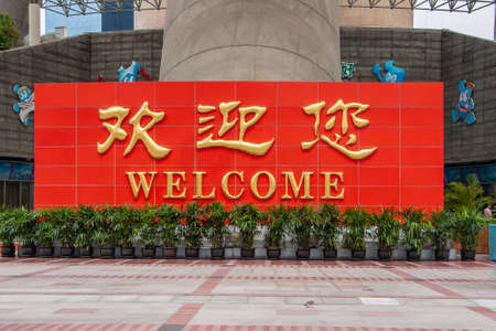 Shanghai, China - May 4, 2010: Pudong, Lujiazui district. gold on red welcome sign at on of the brown concrete support pillars of Oriental Pearl TV Tower behind green plants in pots.のeditorial素材
